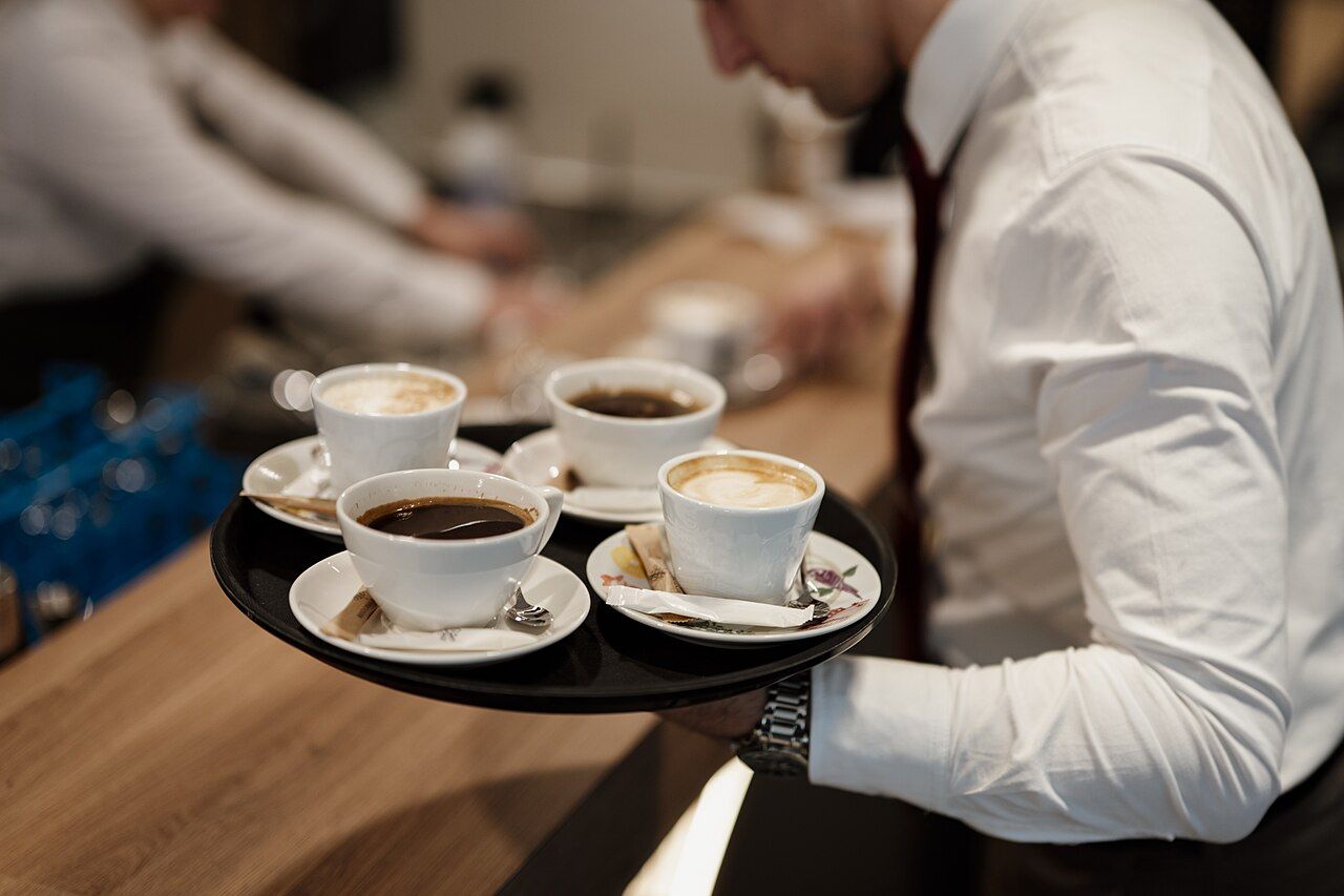 Servicekraft trägt ein Tablett mit Kaffeetassen