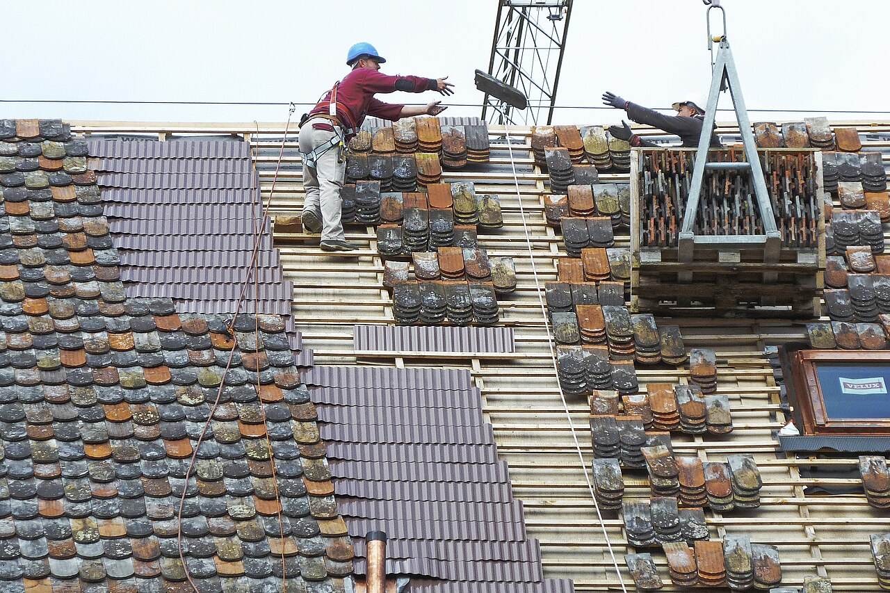 Dachdeckerarbeiten mit Kran und Dachziegeln