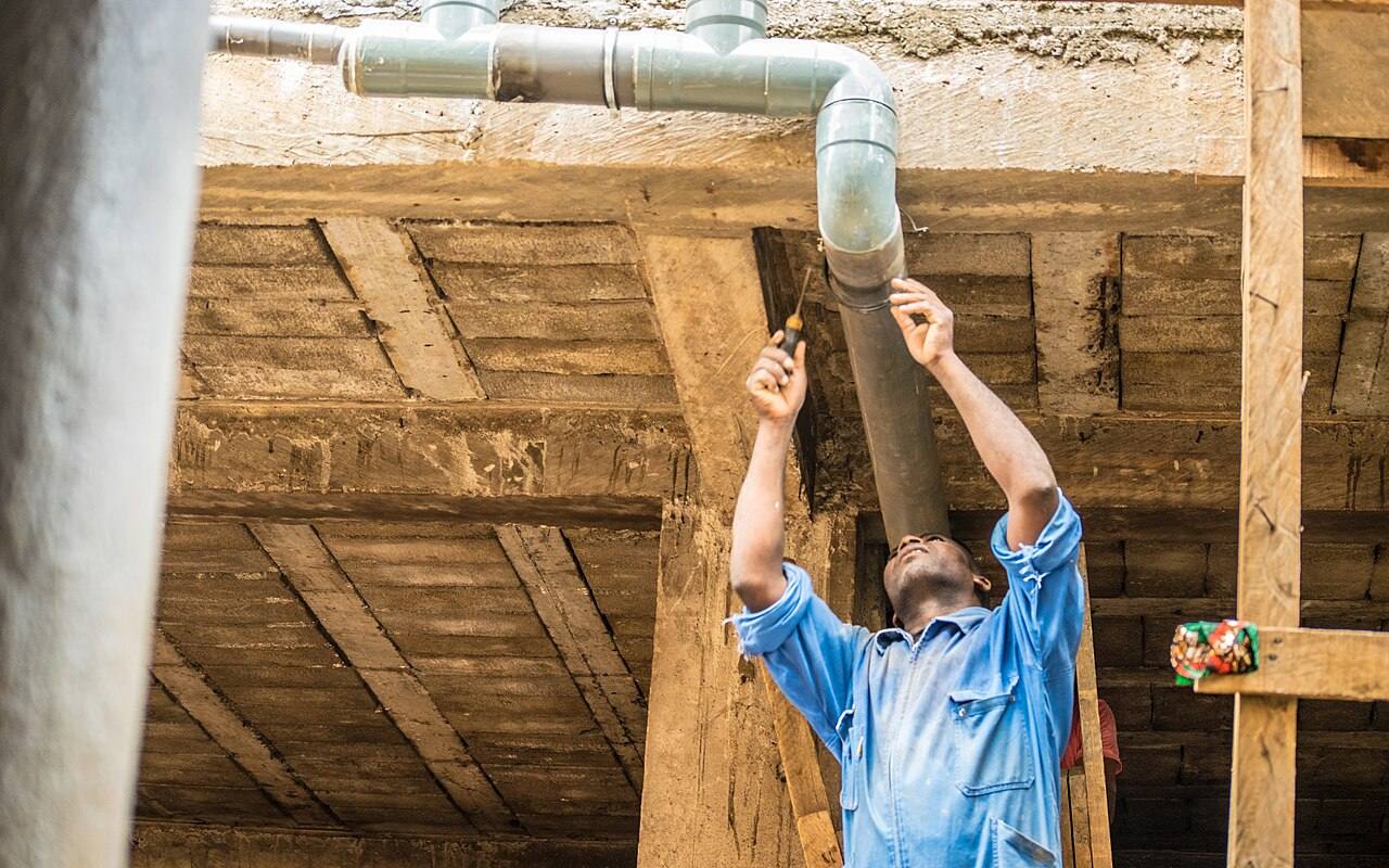 Installateur befestigt ein Fallrohr unter einer Holzdecke
