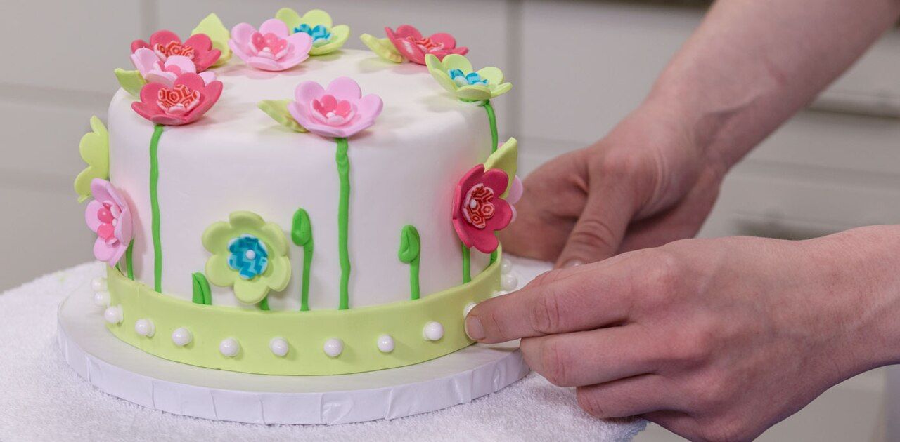 Hände dekorieren eine Torte mit Zuckerblumen