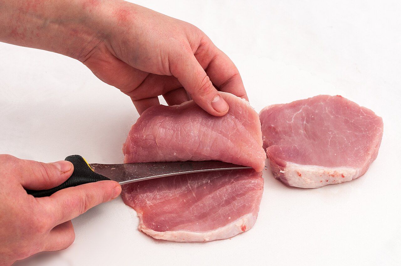 Hände schneiden ein Stück Schweinefleisch