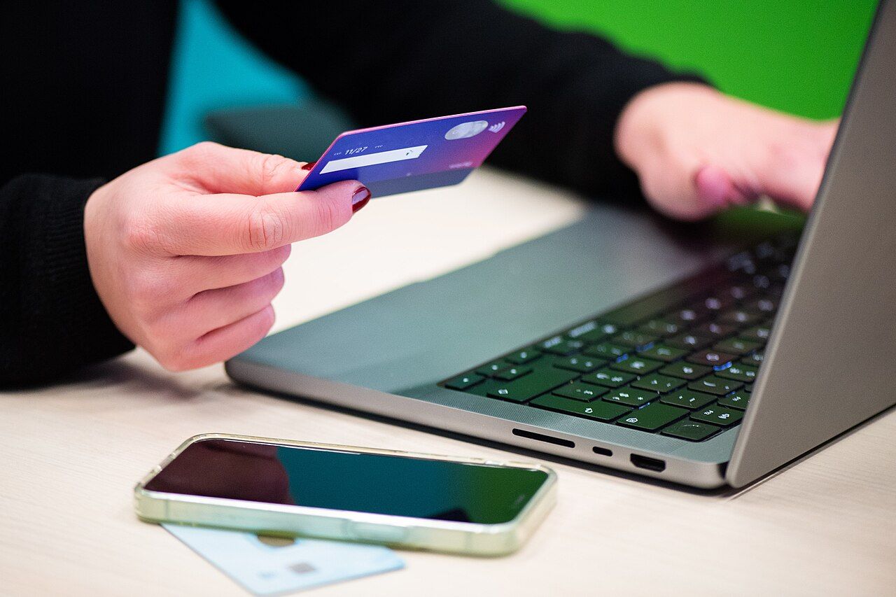 Hände mit Bankkarte vor einem Laptop beim Onlinekauf