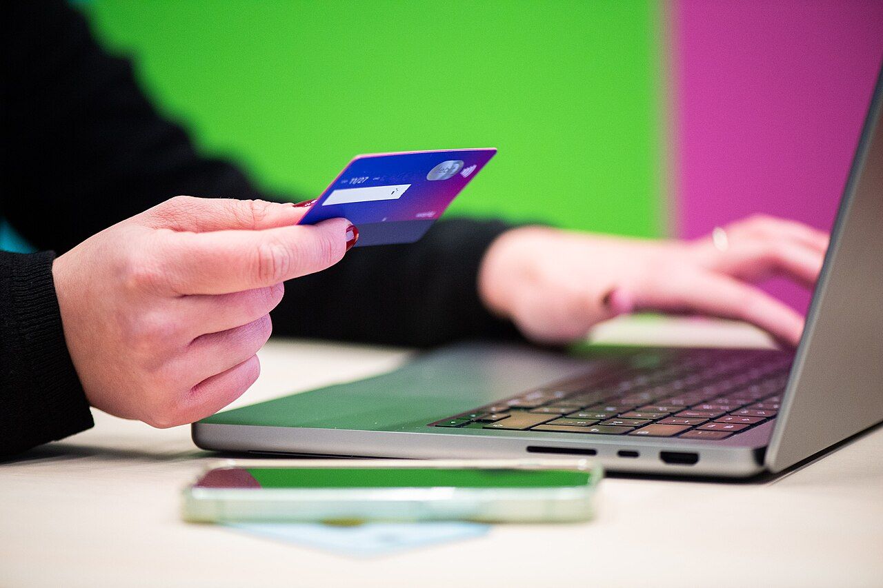Hand hält eine Bankkarte beim Online-Einkauf am Laptop