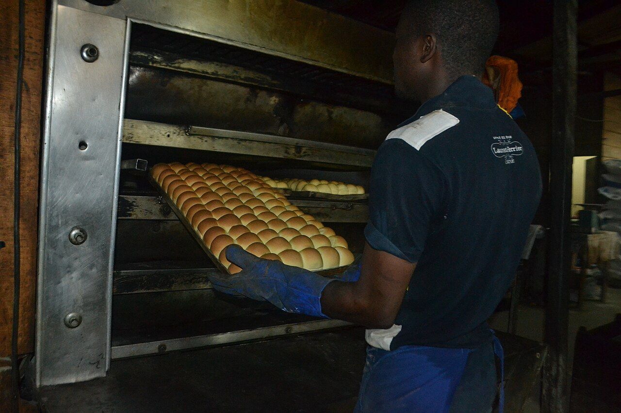 Bäcker mit einem Blech Brötchen am Backofen