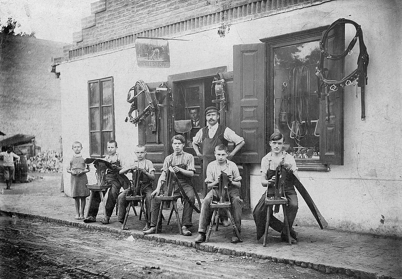 Historische Sattlerwerkstatt mit Lehrlingen vor dem Haus