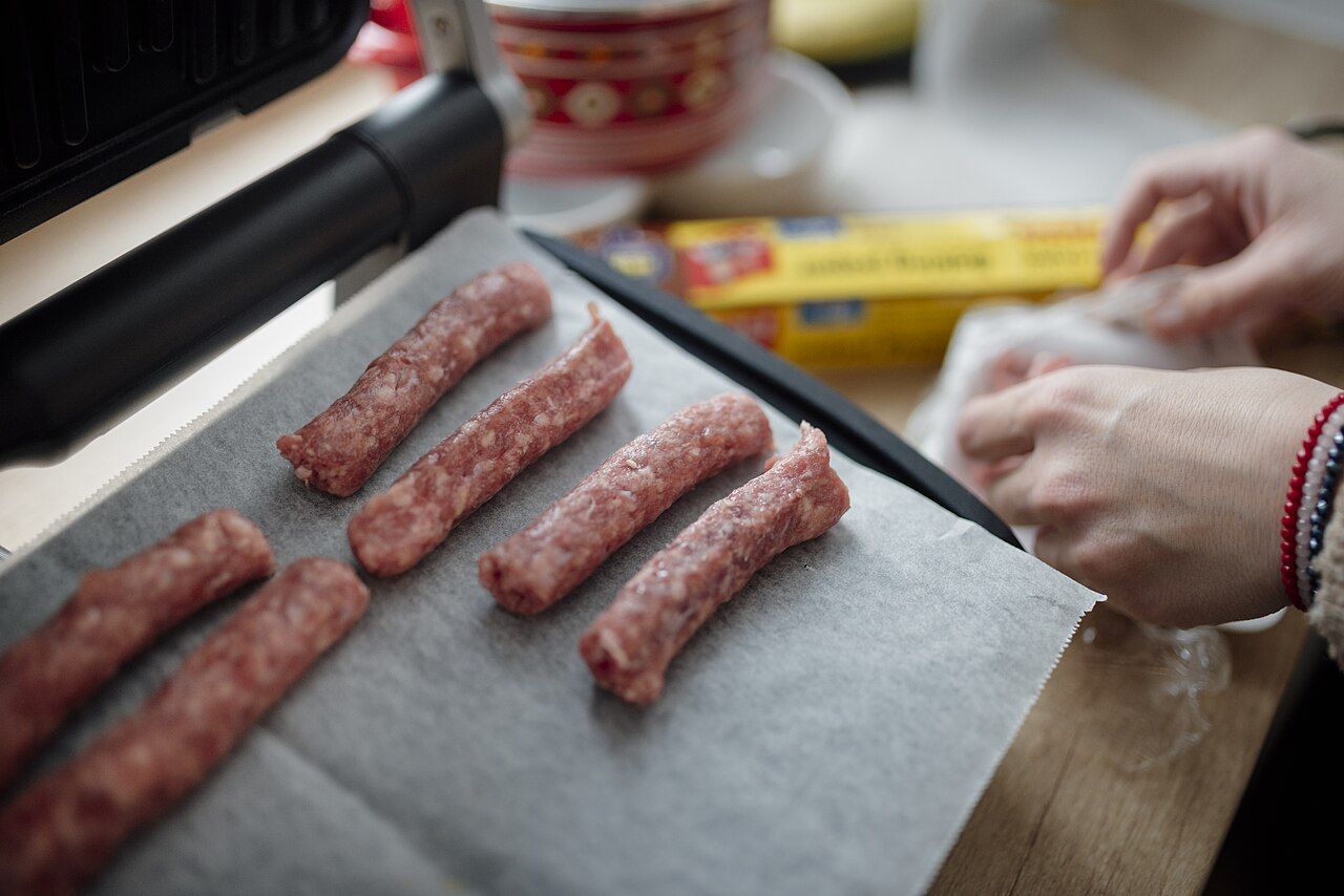 Hände legen Bratwürste auf ein Backblech