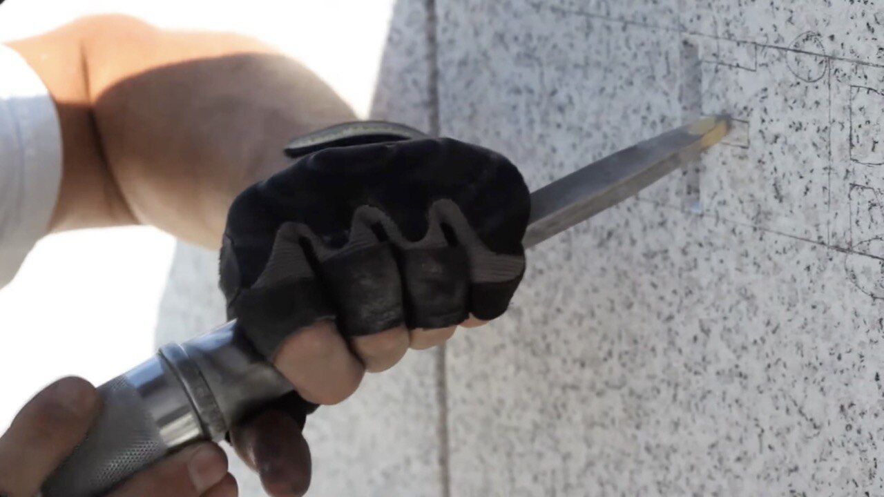 Hand mit Handschuh führt einen Meißel an einem Steinblock