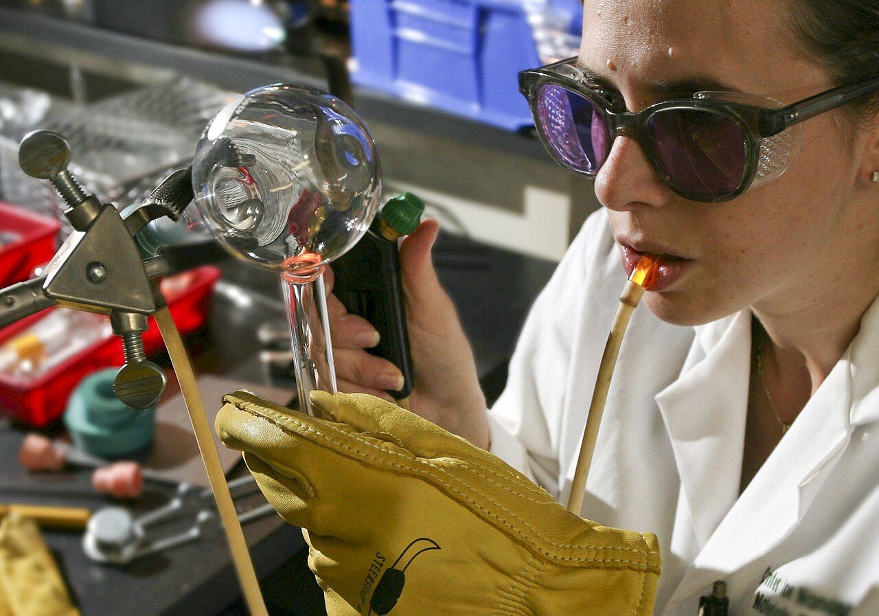 Glasbläserin mit Schutzbrille bei der Arbeit an Laborglas