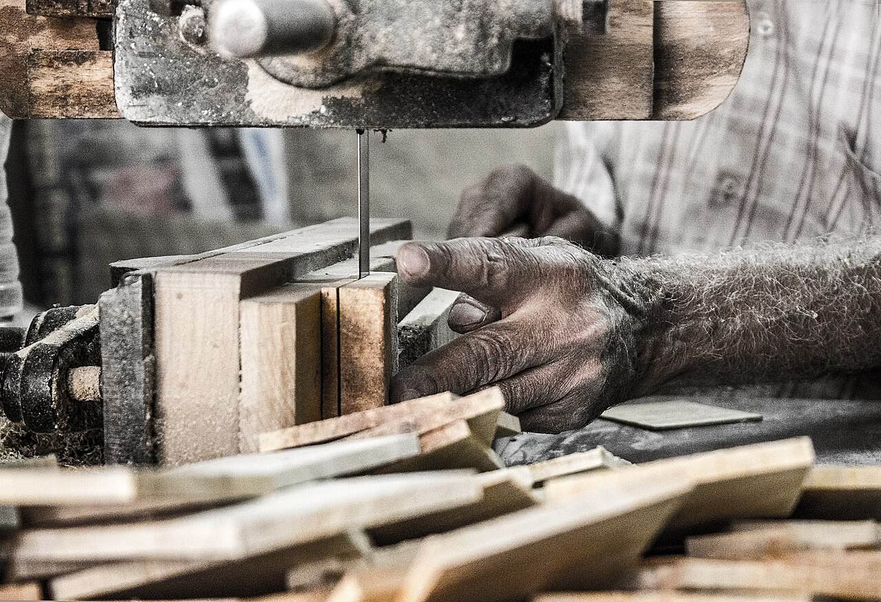 Hand führt Holz an einer Bandsäge