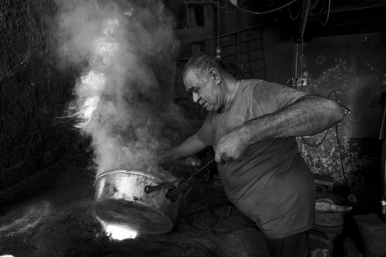 Handwerker erhitzt ein Metallgefäß über Feuer
