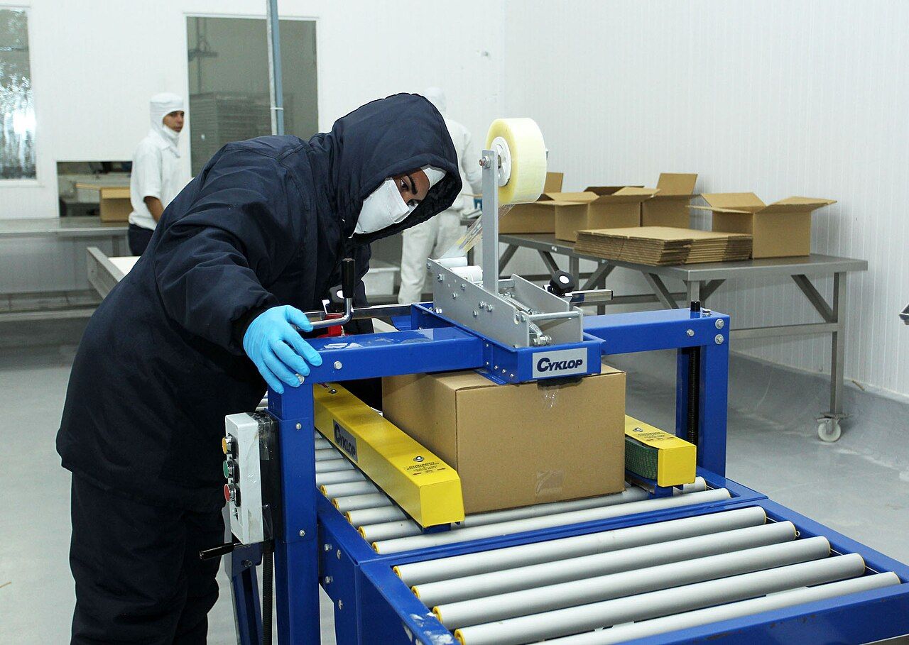 Mitarbeiter verschließt einen Karton an einer Verpackungsanlage