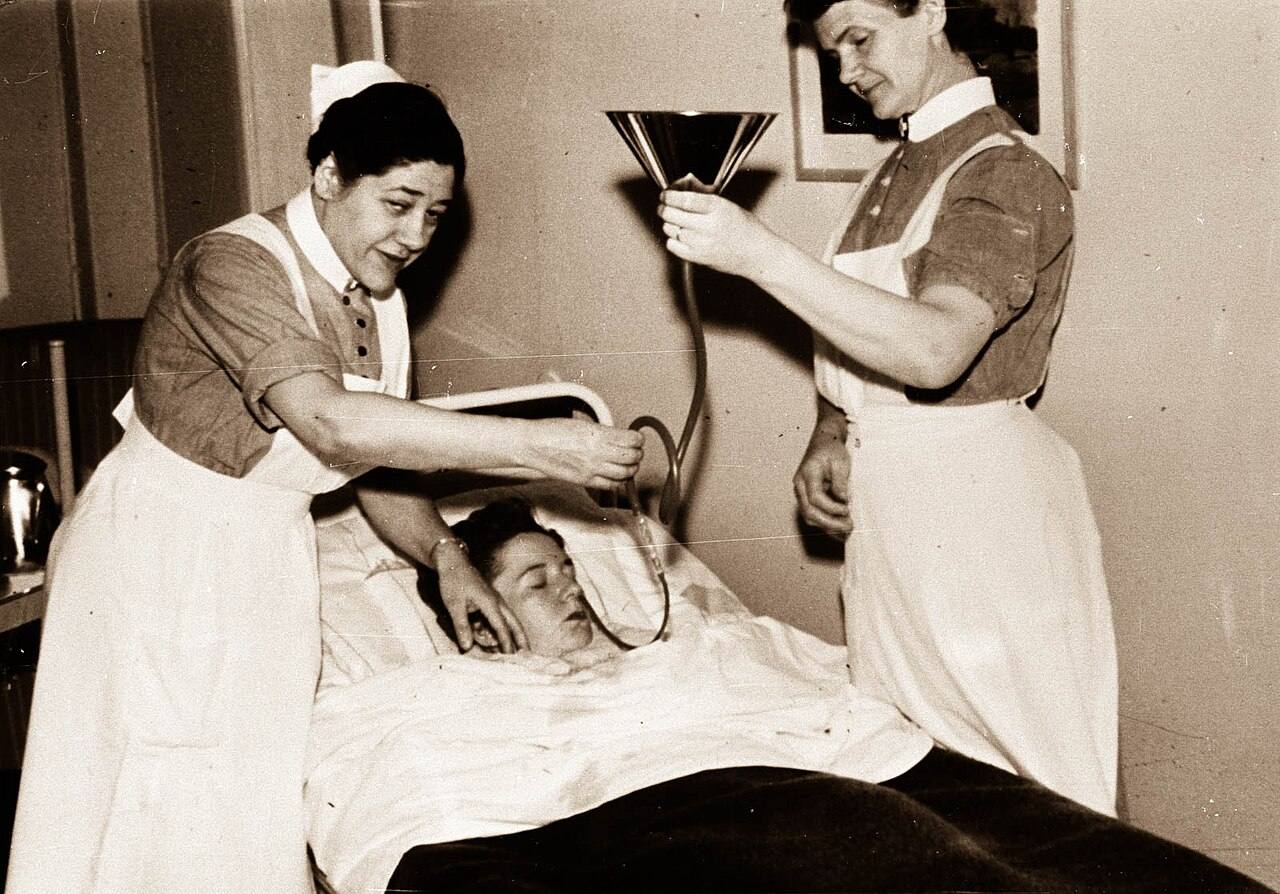 Historische Aufnahme zweier Pflegerinnen am Krankenbett