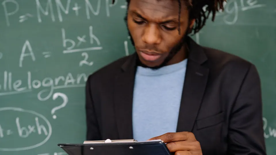 Lehrer am Klassenzimmer-Tafelbild prüft Unterlagen auf einem Klemmbrett