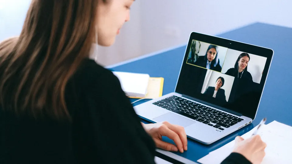 Frau führt am Laptop eine Videokonferenz und macht sich Notizen