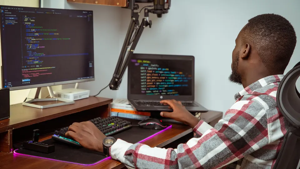 Software-Entwickler arbeitet an Laptop und Monitor mit Programmcode im Buero