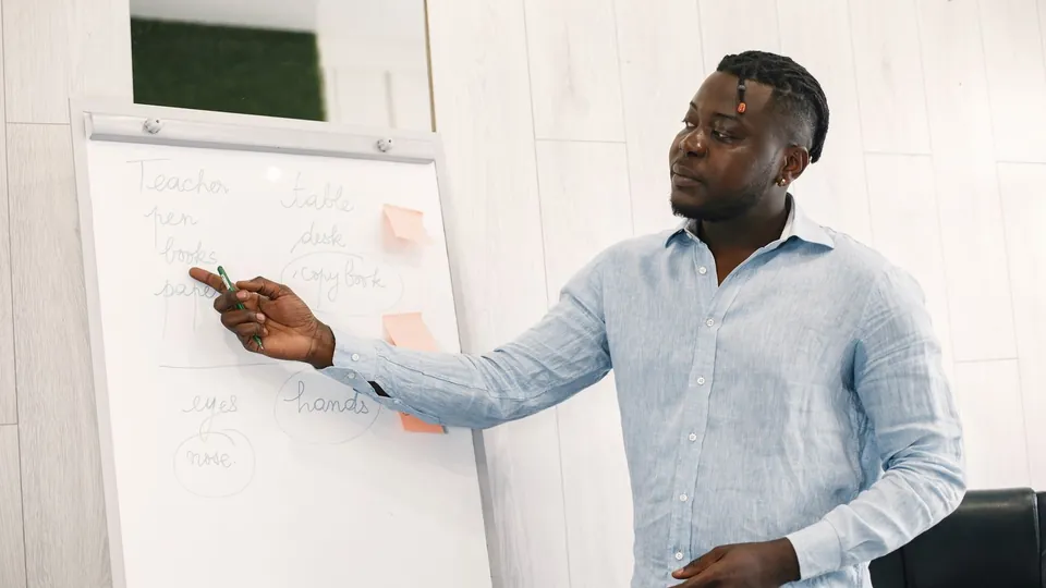 Lehrer zeigt mit einem Stift auf Wörter auf einem Flipchart im Unterrichtsraum.