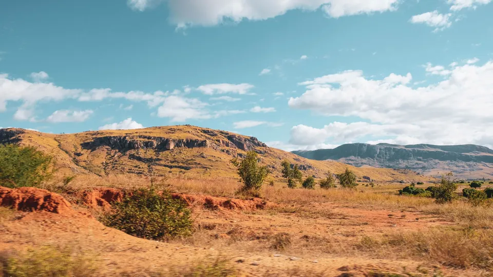 Grasland und rote Erde vor einem Bergzug im Hochland von Madagaskar.