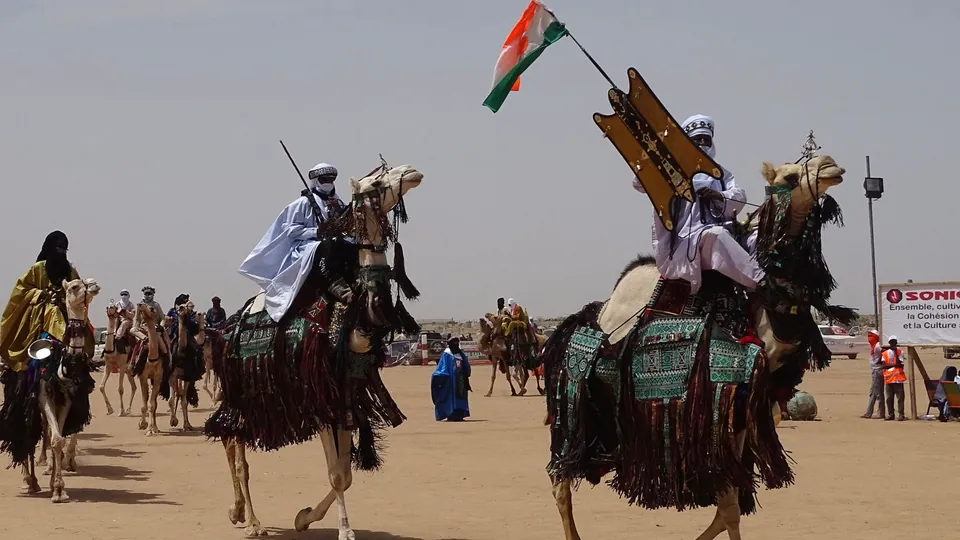 Reiter auf geschmückten Kamelen mit Nationalflagge bei einem Festival in Ingall, Niger.