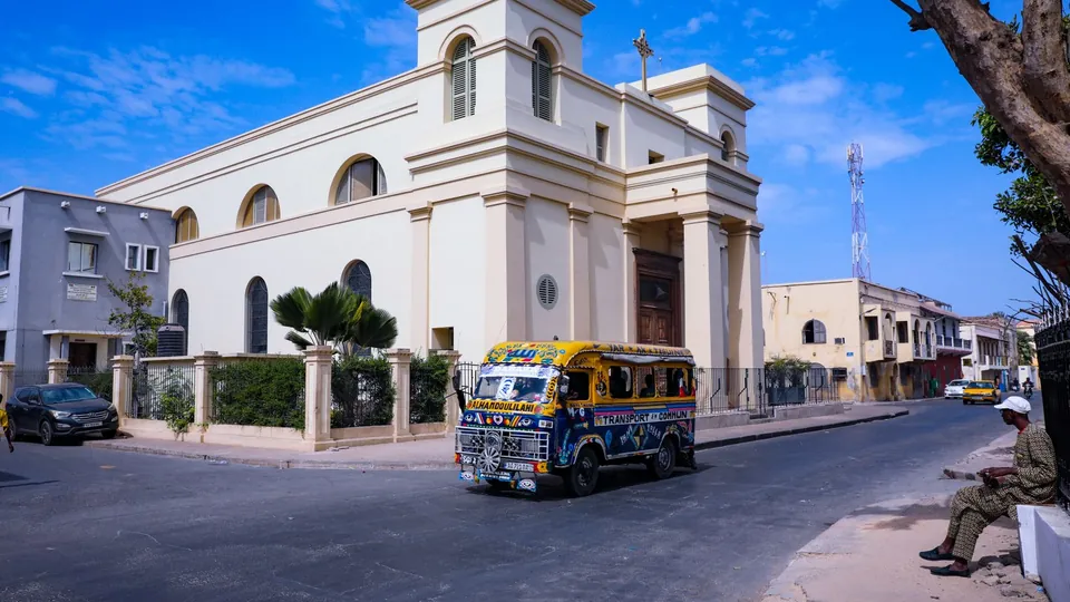 Weißes Kirchengebäude in Dakar mit einem bunten Minibus auf der Straße, Senegal.